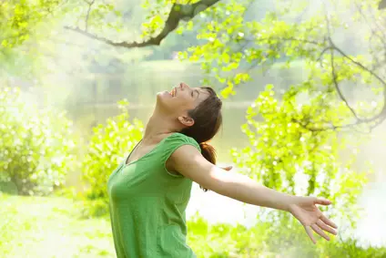 Femme épanouie qui ouvre les bras au monde dans un cadre verdoyant