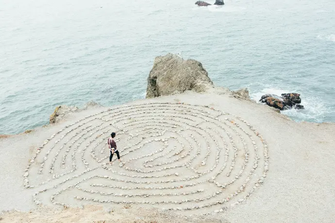 personne marchant sur la plage, un labyrinthe est dessiné sur la plage